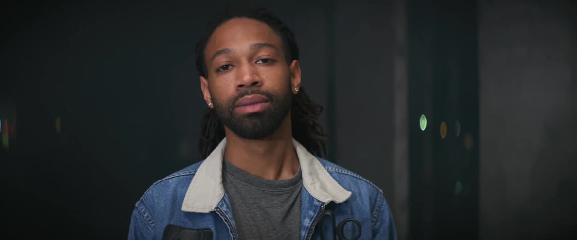 Black man wearing jeans jacket standing at a dark room while a red laser scam his body