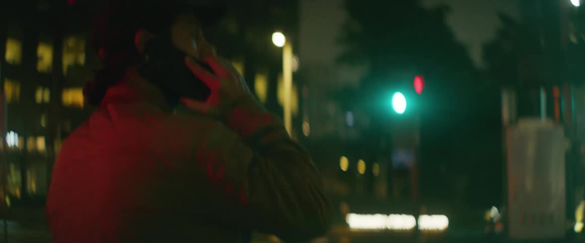 A man talks on the phone while walking through a city at night