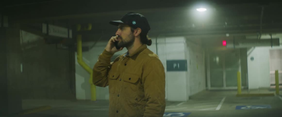 Man wearing quilted jacket makes phone call as he walks through parking area