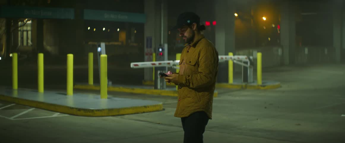 Man wearing a baseball hat and a jacket uses a smartphone on the city street at night