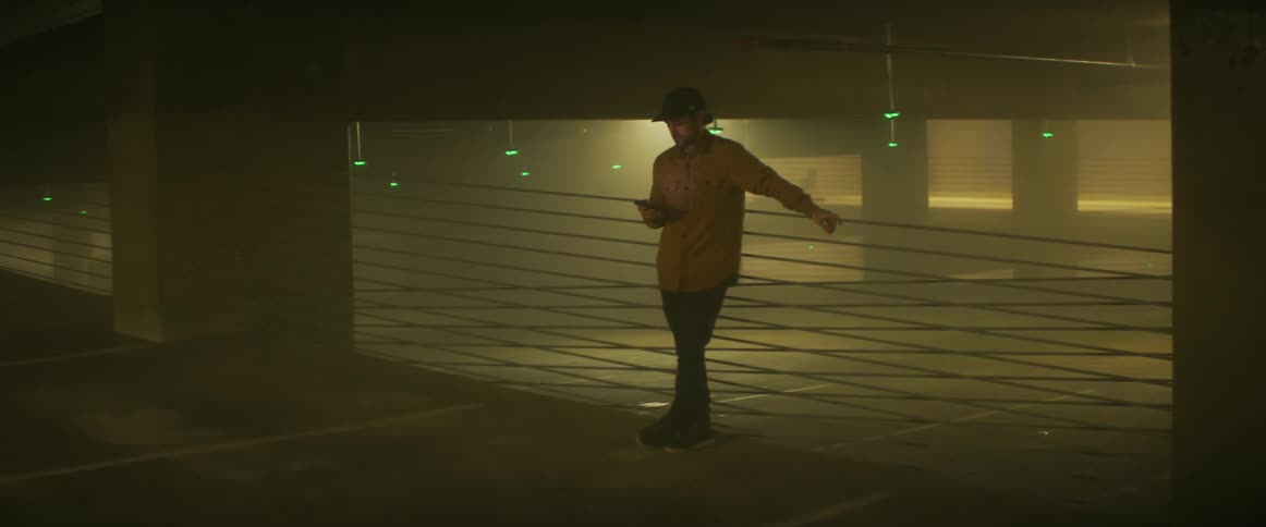 A man looking at a smartphone while standing inside a dark parking garage