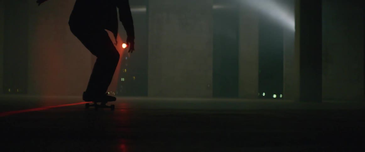 Skateboarder rides board along concrete near building at night