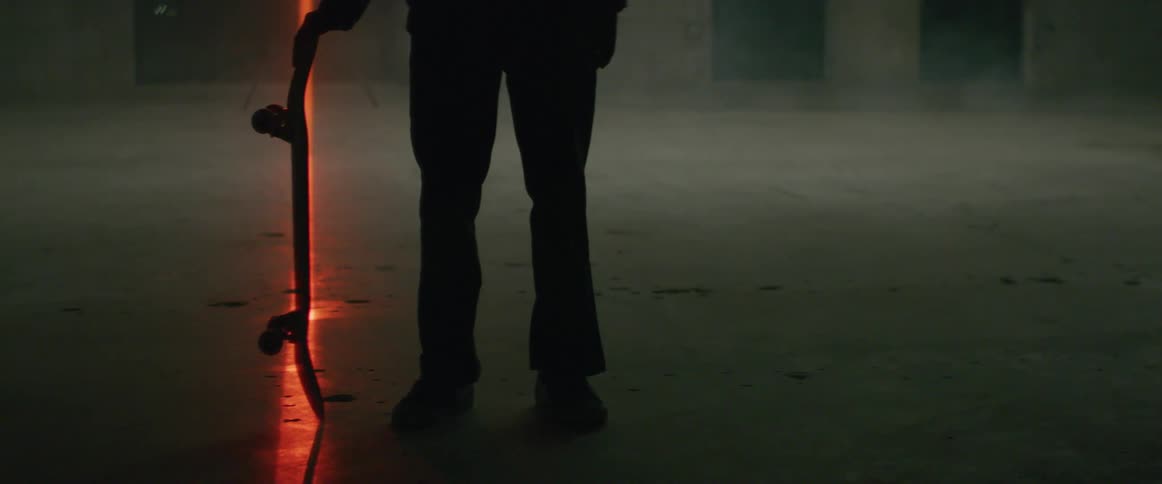 Person stands in foggy area near building rotating skateboard on red laser line