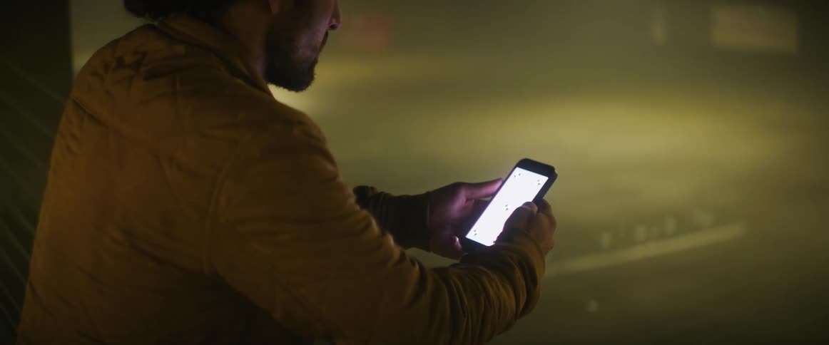 A man uses his smartphone while leaning against the railing in a parking garage