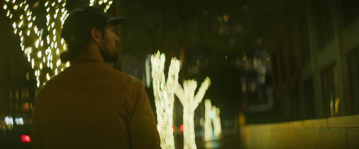 Man wearing a baseball hat and a jacket walking on the city street at night