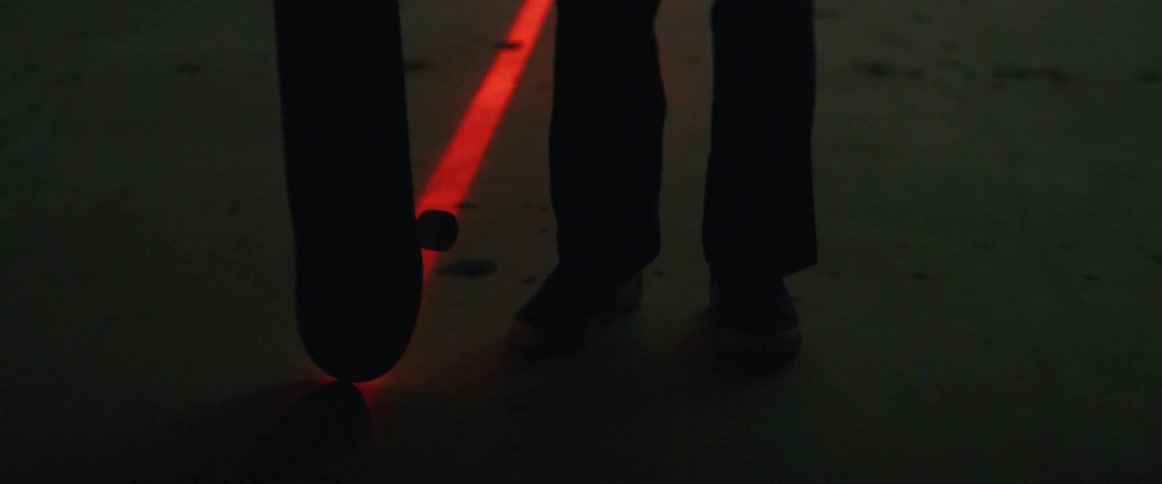 Person standing silhouetted rotatesskateboard on line made across concrete by red laser