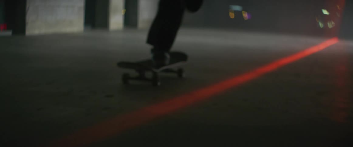 Silhouette of a man over a skateboard inside a room with a red laser line on the floor