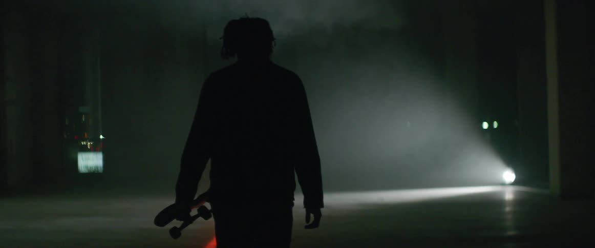 Man holding a skate board walking at an empty dark room