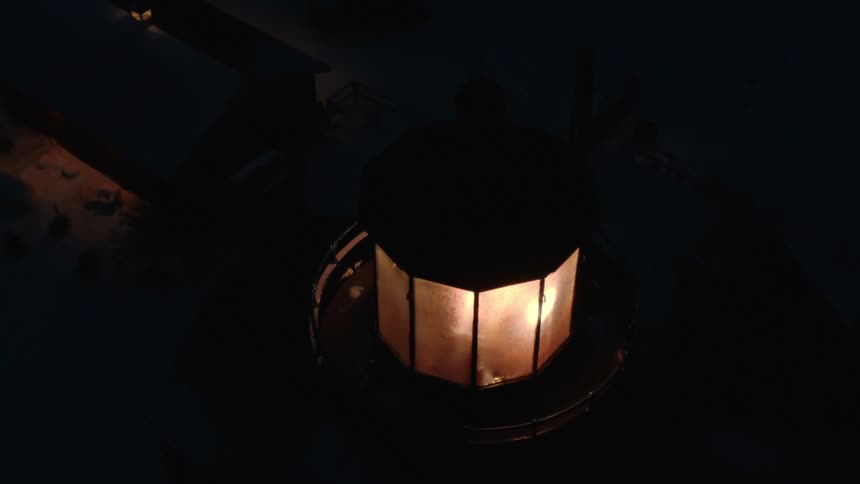 Beacon rotates on top of lighthouse as light shines from nearby building