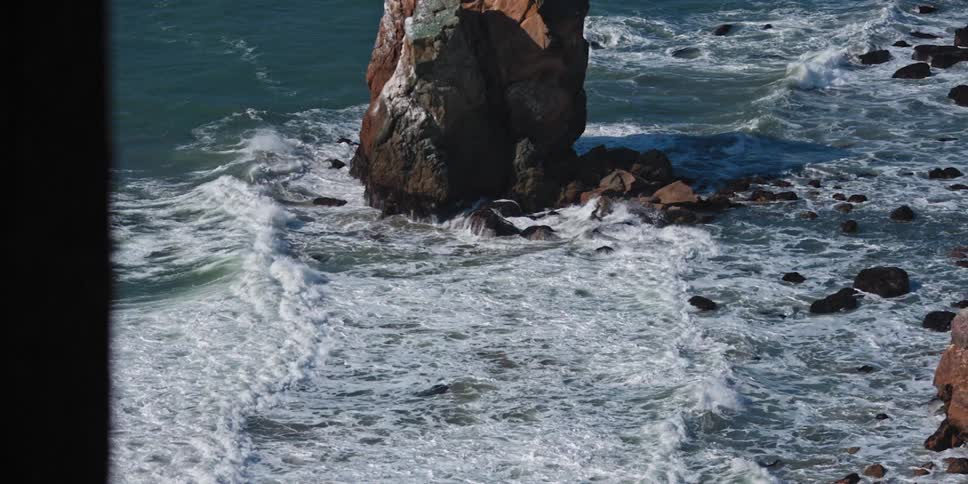 Waves roll past boulders foaming as they reach the shore