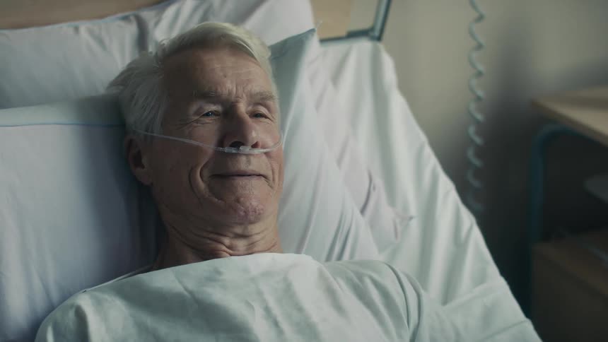 Old man lying in a hospital bed and nodding at someone