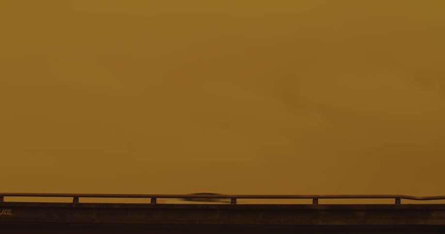 Cars are traveling on a busy highway under a yellow sky