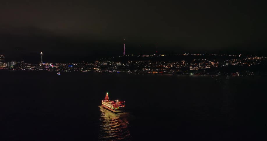 Following behind a boat with bright colorful lights heading towards the Seattle skyline along Lake Union