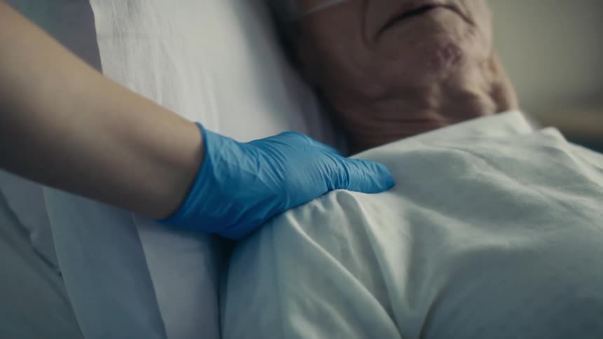 Person wearing glove touches hospital patients shoulder to comfort him