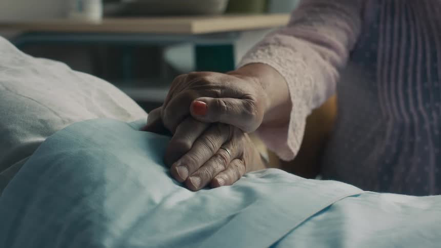 Old woman touching the hand in a caring way of an old man lying in a hosital bed