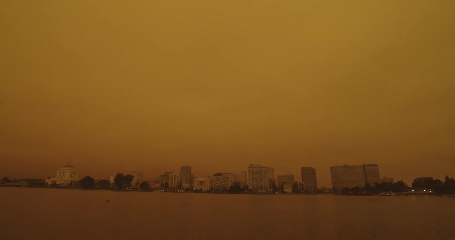 City skyline sits near ocean under an amber sky