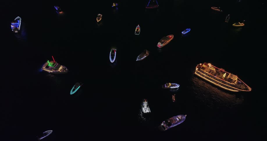 Pullback reveal over boats and yachts lit up in different colors at night