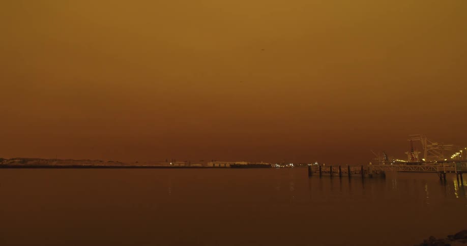 Waterfront lights reflect from water under sky tinted with afterglow
