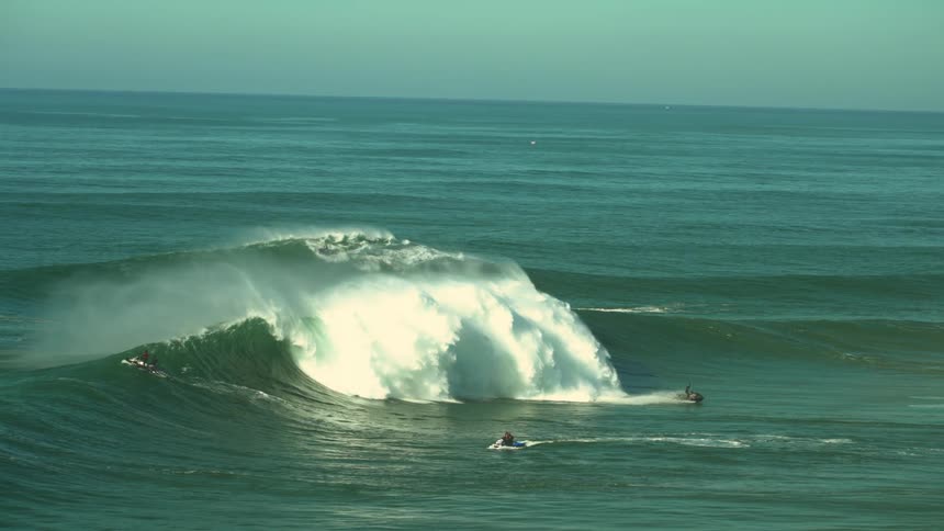 Big waves hitting the coast while people are surfing and driving their jet skis