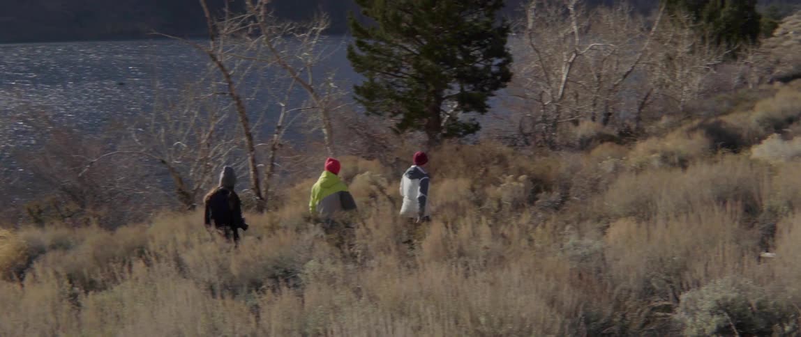 Three People Walking Through Tall Grass Beside a River in a Peaceful Outdoor Journey.