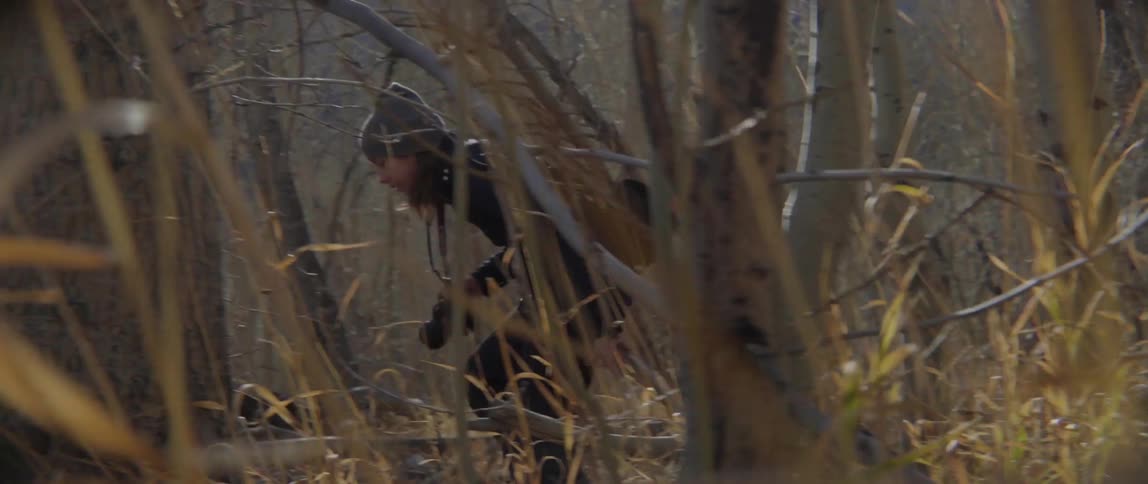 A woman carrying a camera is wading through a dense forest