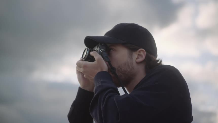A man raises his camera to take a photograph while standing outdoors during the day