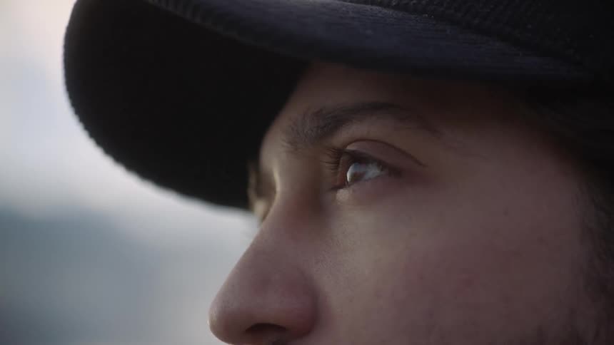 Man standing outdoors wearing a baseball cap opens his eyes