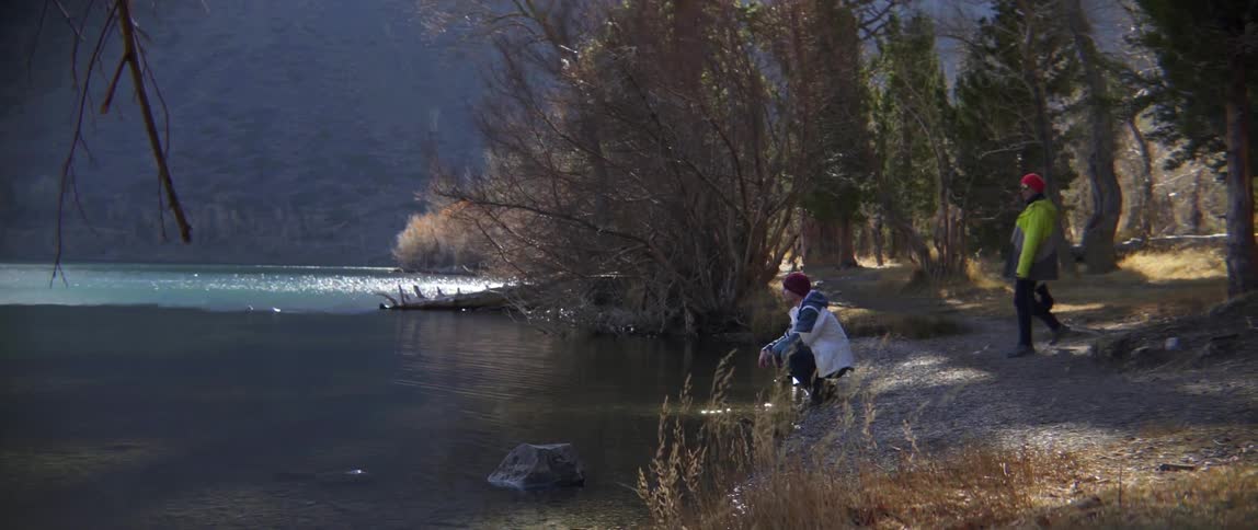 Man Tossing Rocks Into Water Is Joined by Another Person in Playful Calm.