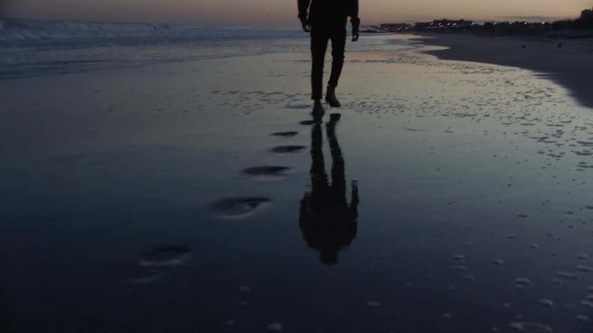 Man walks near water as wet sand reflects his figure