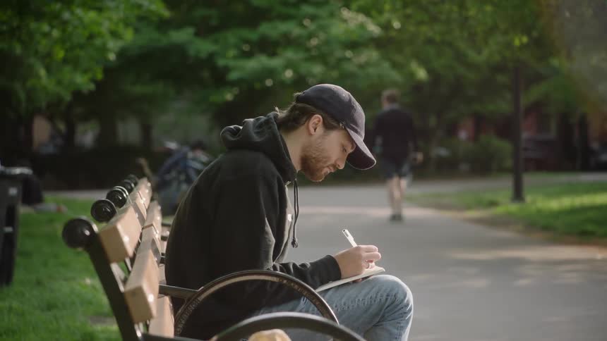 A man is sitting on a park bench writing in a book