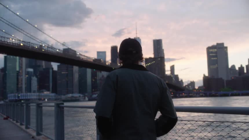 A man walks on a pedestrian bridge beside a river and large city