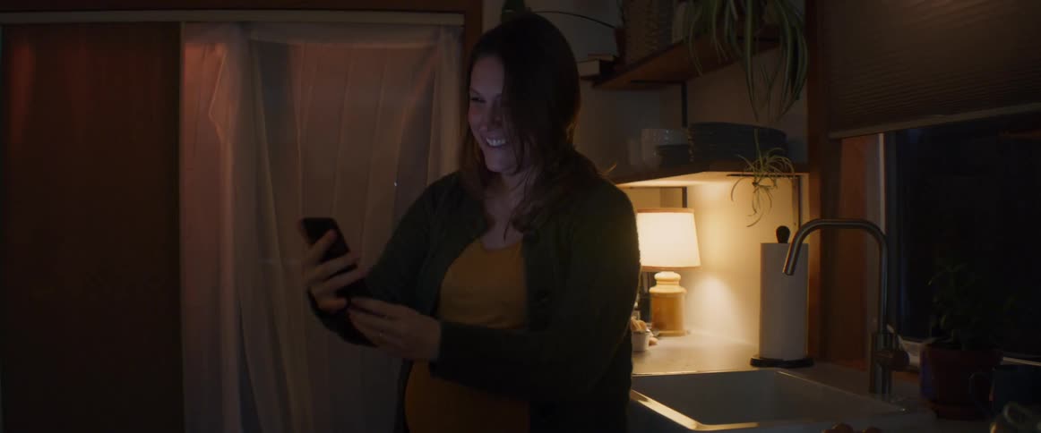 Happy pregnant woman shows her belly on a smartphone call in the kitchen at home