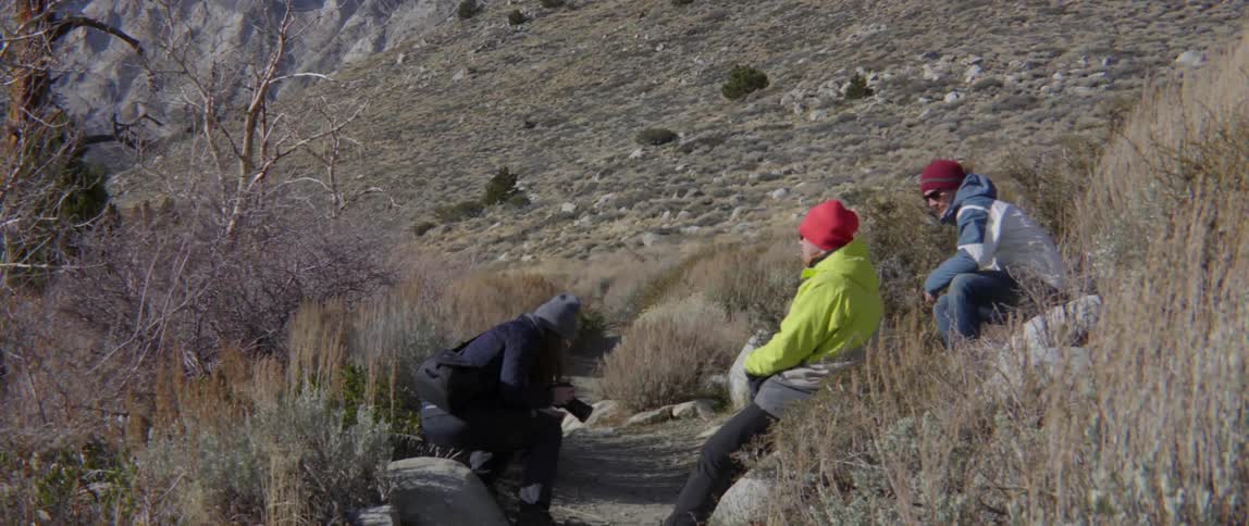 Three people take a break from hiking and sit beside path