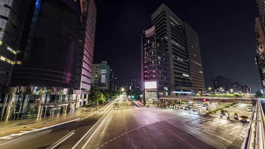 Traffic flows through intersection in downtown city as large screen image on building changes
