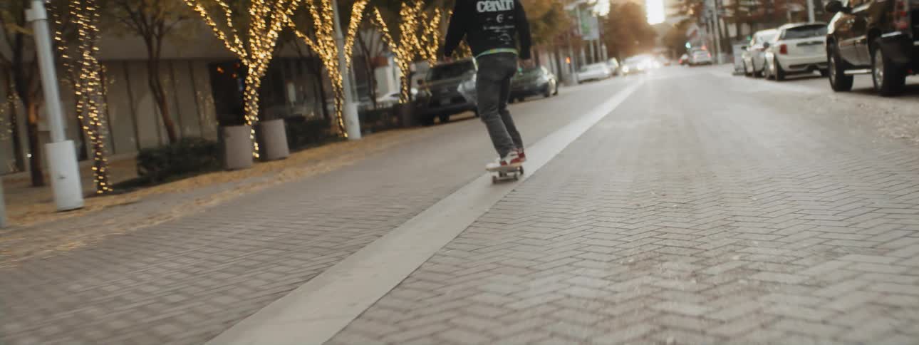 Skateboarder rides board along street passing parked cars