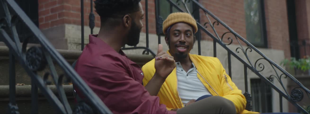 Two men talking while sitting on the front stoop of a brick building