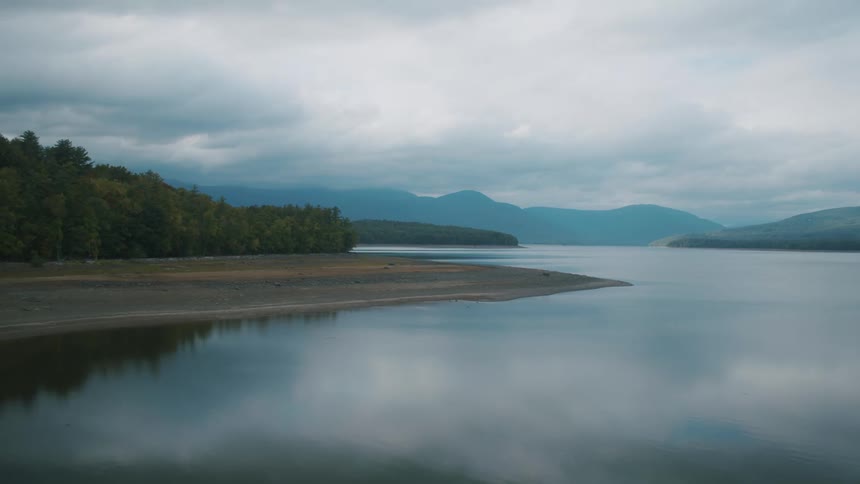 The sky and clouds reflect off a calm lake by a forest