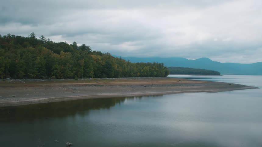 Trees on shore are reflected in the lake surface on a cloudy day