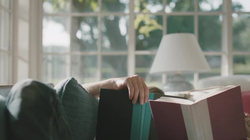 A man lying on a couch reading next to a child both hidden by hardcover books