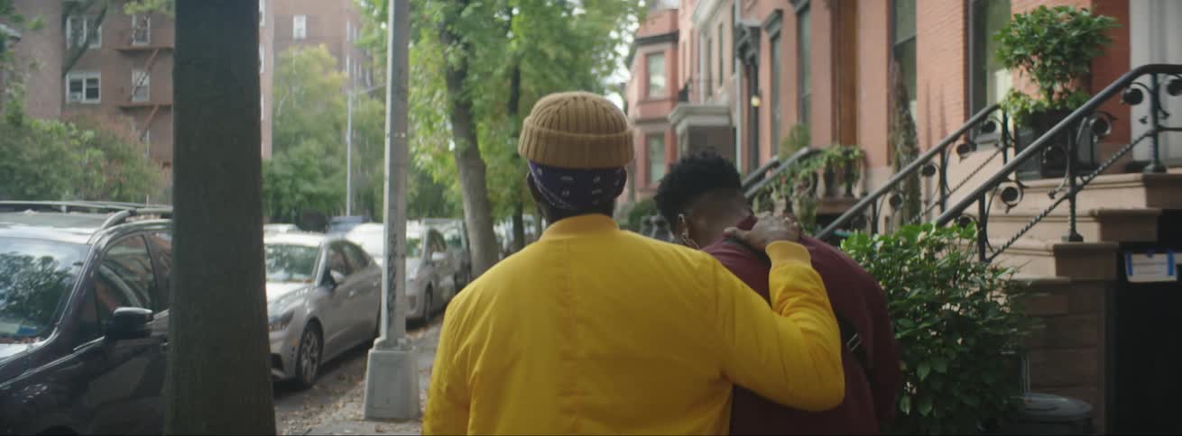 A man rubs his partners neck as they walk down a city street through a neighborhood