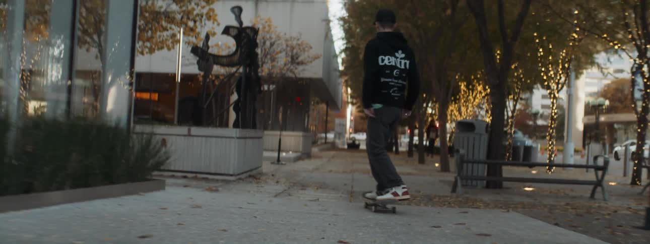 A teenage boy skateboards down a city sidewalk past a woman walking
