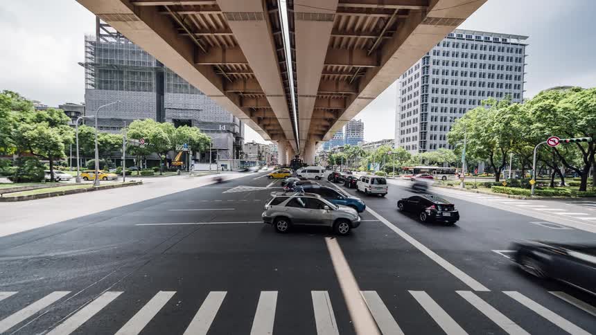 Cars and trucks stop under an overpass before continuing through a busy intersection