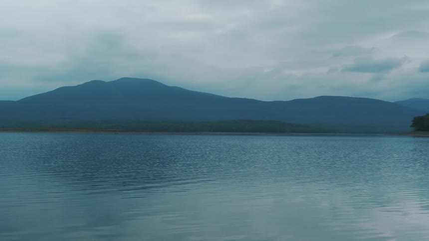 Clam surface of a lake near the mountains on an overcast day at evening