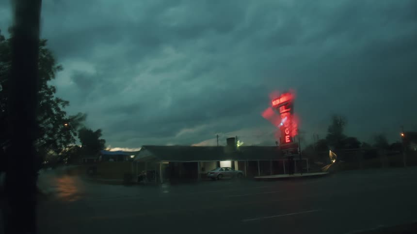 A car driving by a small motel on a rainy cloudy night