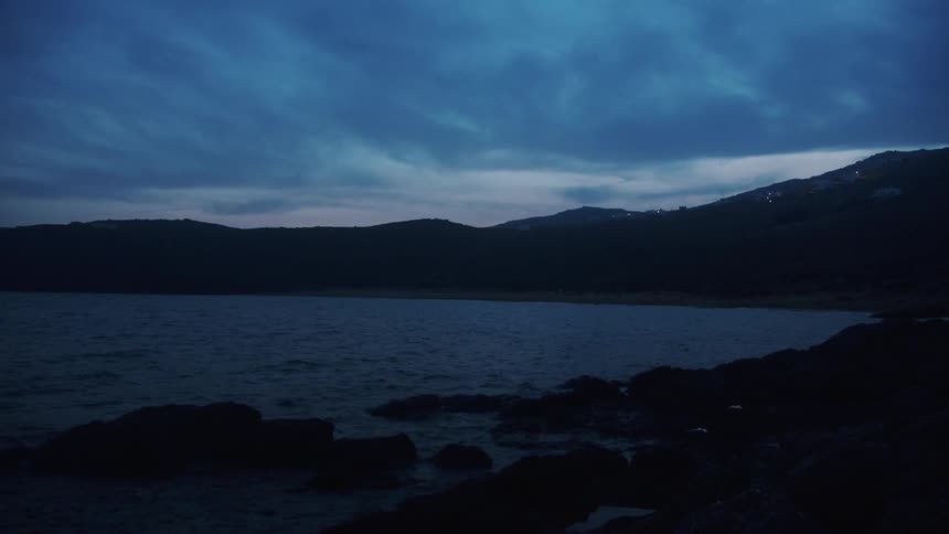 Calm surface of a lake near the coast close to the mountains at evening