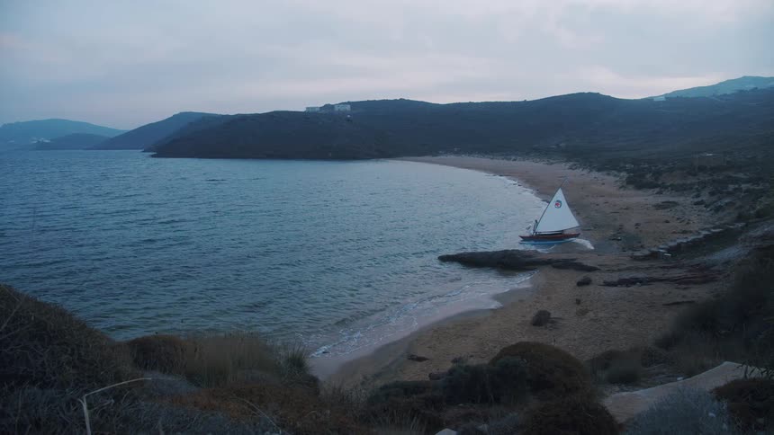 A man walks towards a sailboat on the shore