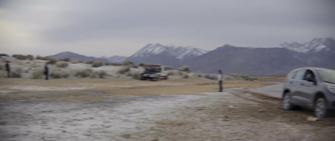 A tow truck is parked by a stranded car as people watch on