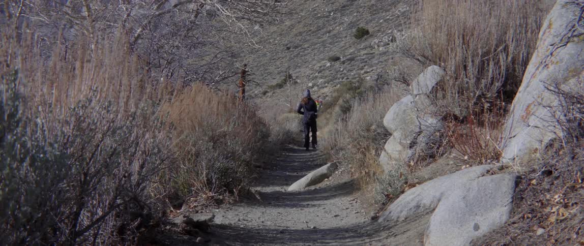 People hiking down trail toward steep hill with adventurous natural movement.