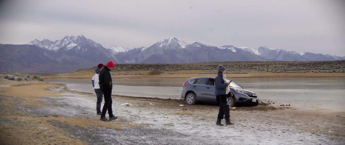 Three people stand before a crashed vehicle on a cloudy day