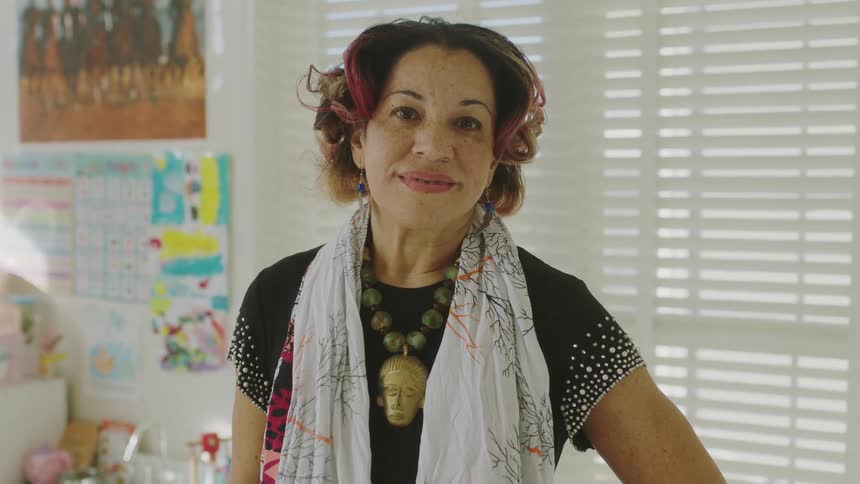 A fashionable woman stands posed with a soft smile with childrens artwork and supplies behind her